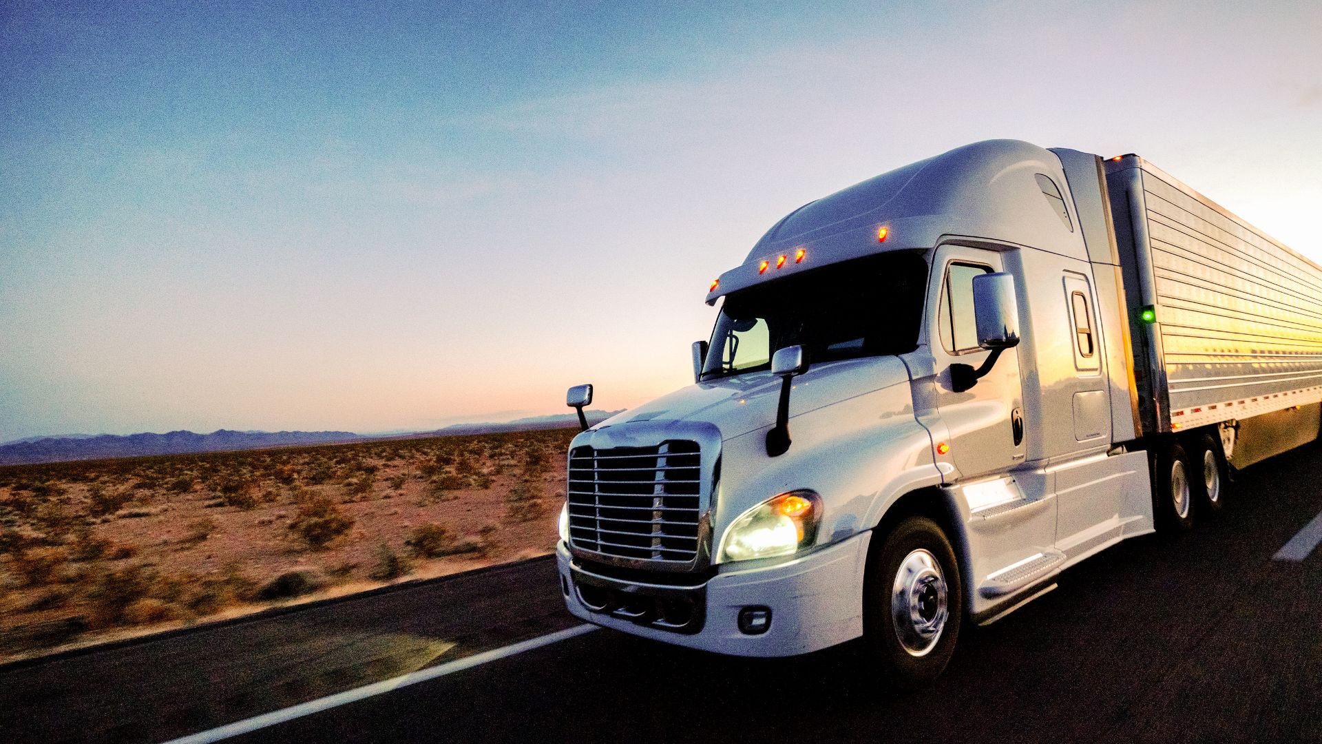 White semi-truck driving on desert highway at sunset