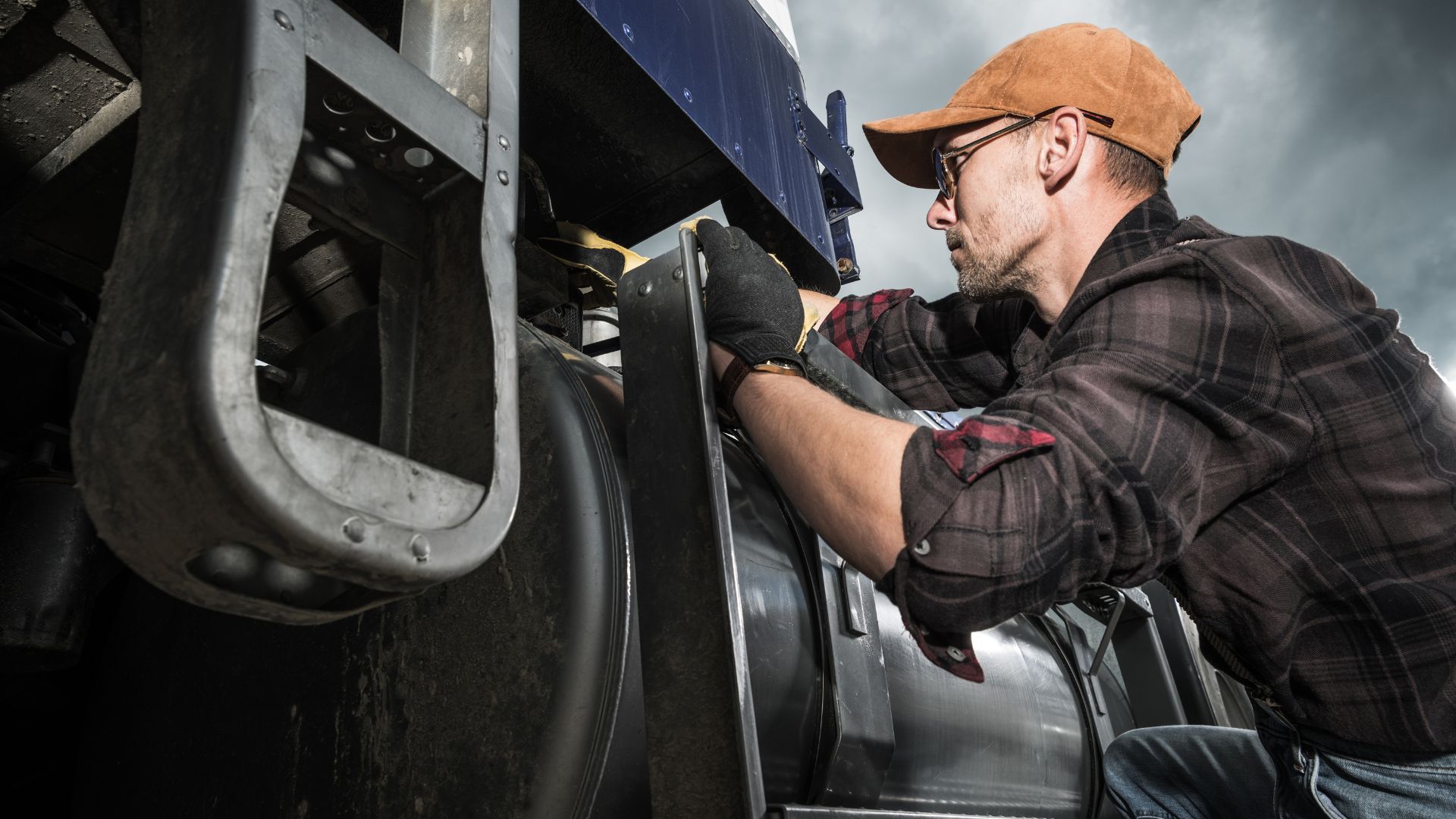 Worker in cap and glasses repairing industrial machinery with gloved hands