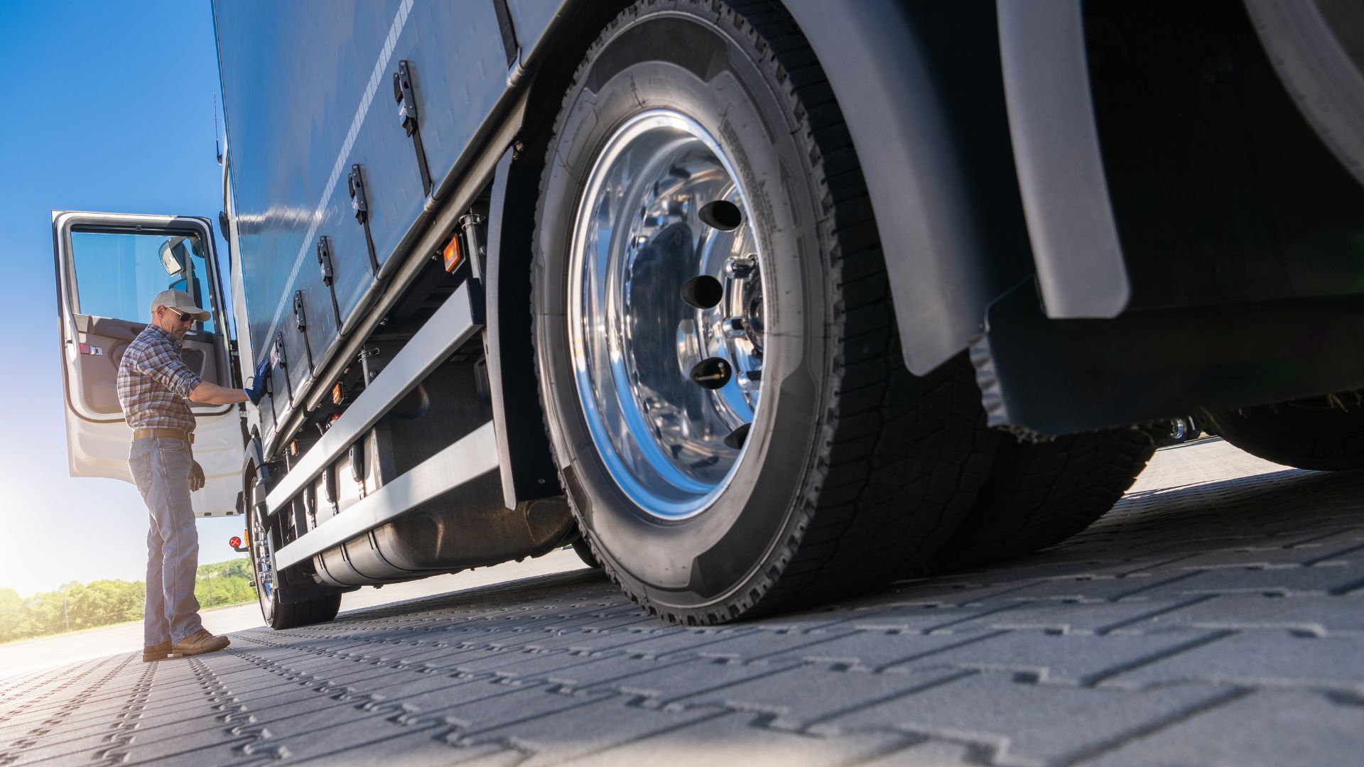 Truck driver inspecting large commercial vehicle tire on loading dock