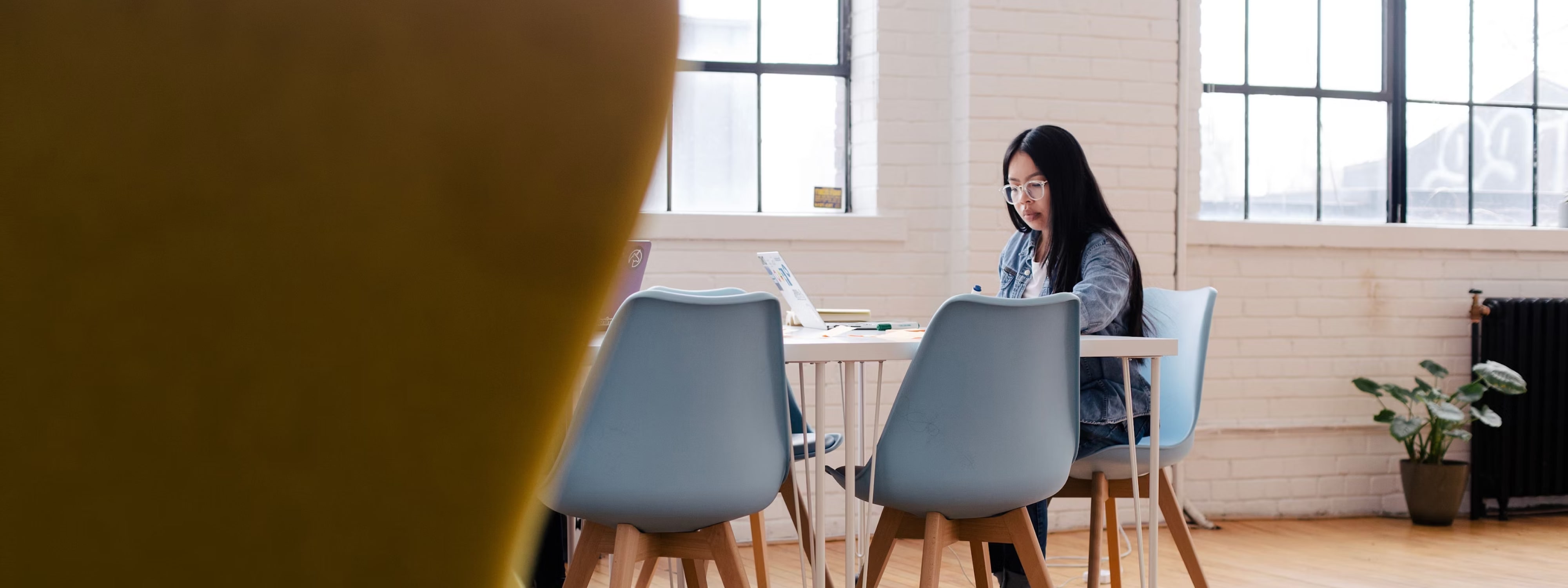 Woman working at a white table with blue chairs in bright office space